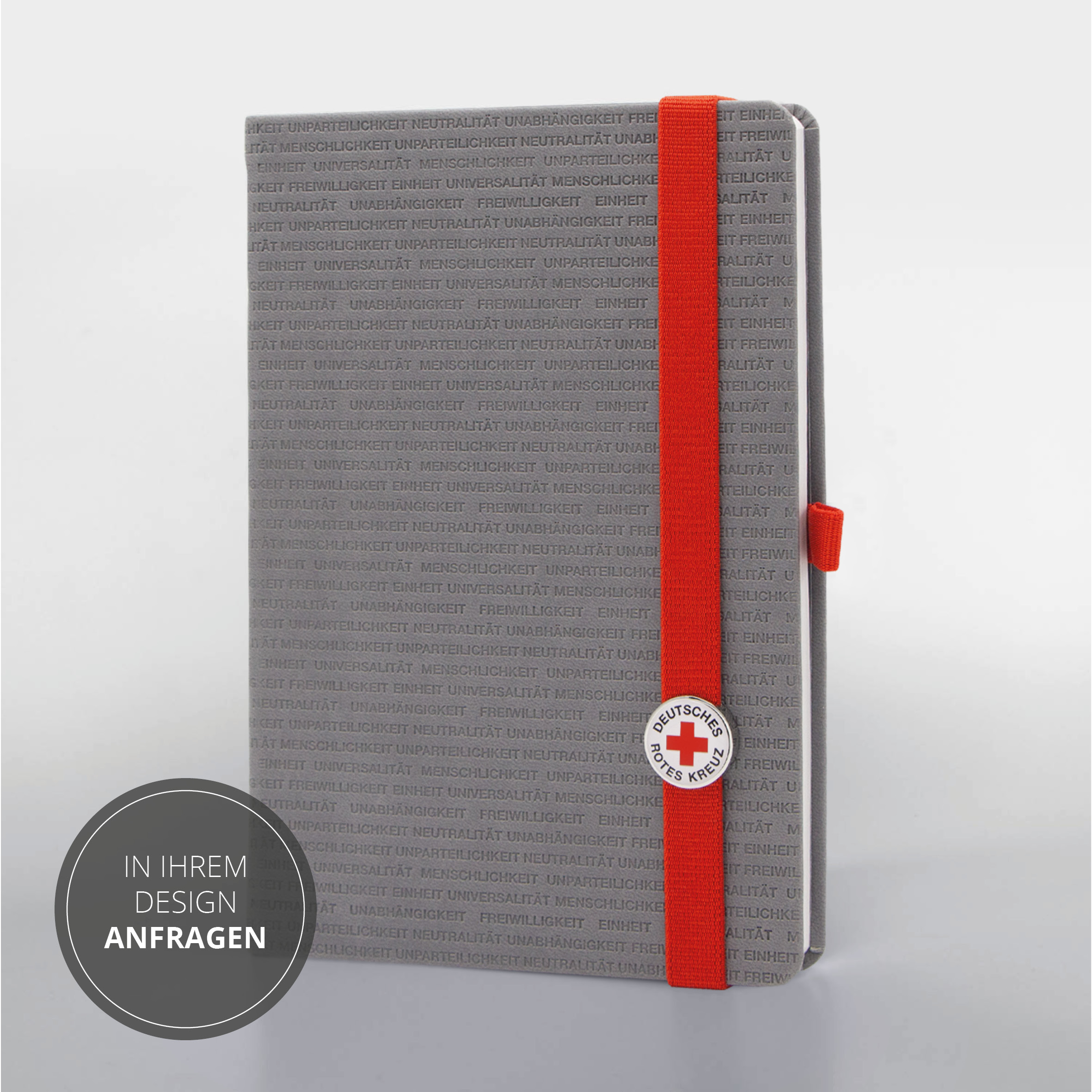 Vorderseite des Notizbuchs mit rotem Lanyband®, DRK-Button und geprägtem Schriftmuster.