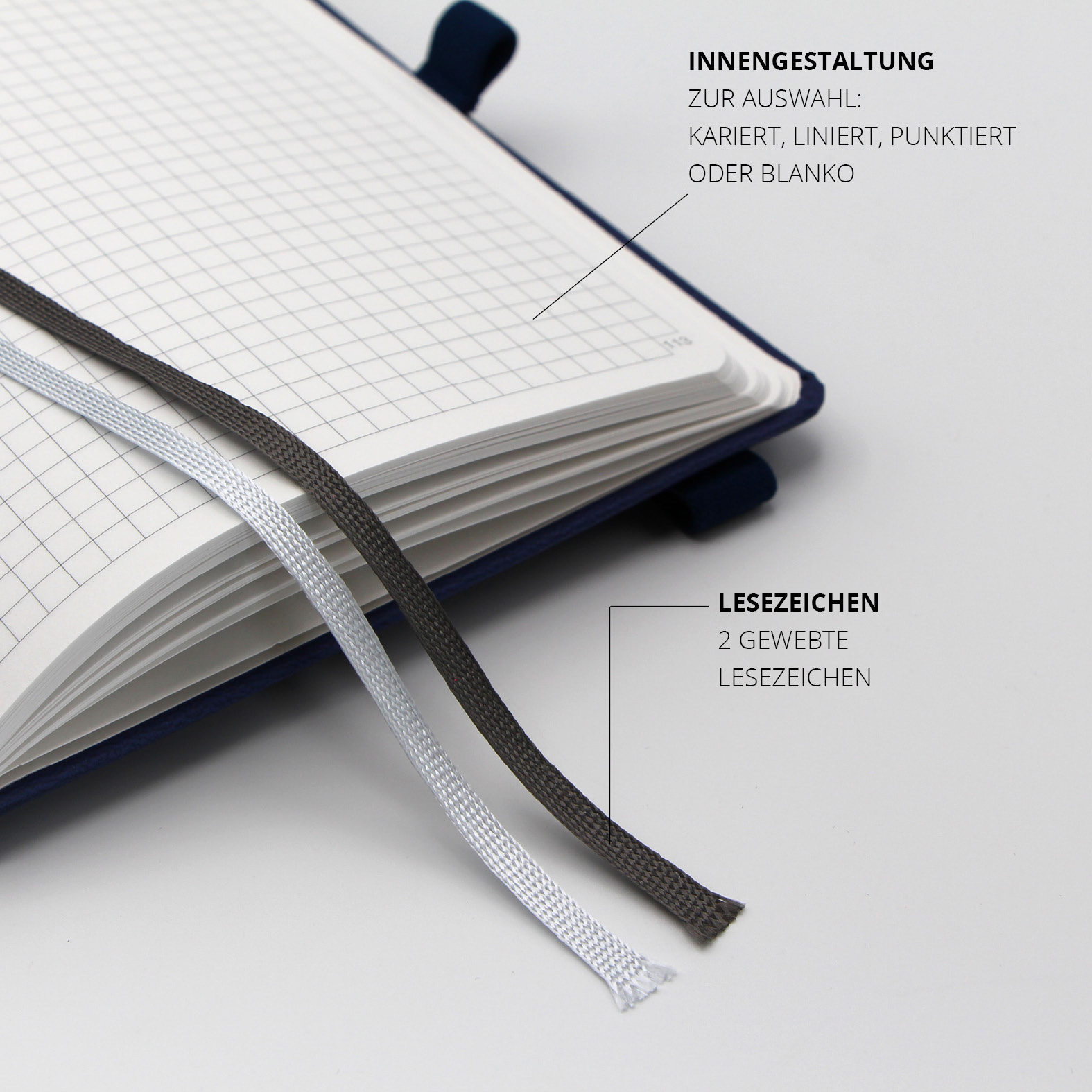 Zwei gewebte Lesezeichen in Silber und Anthrazit im aufgeschlagenen Notizbuch mit kariertem Raster.