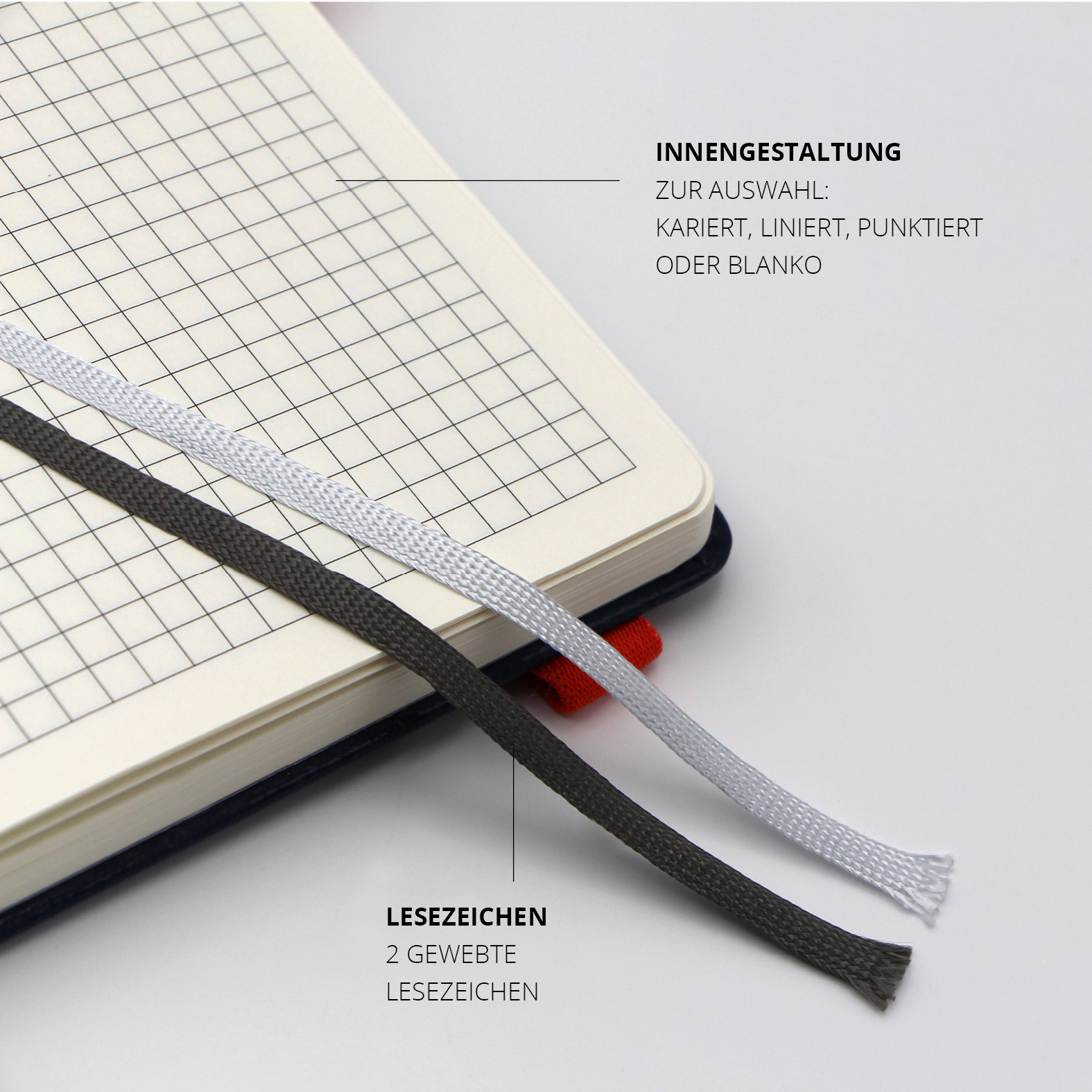 Geöffnete Doppelseite mit kariertem Layout und zwei gewebten Lesezeichen in Weiß und Schwarz, rotes Lanyband® an der rechten Kante sichtbar.