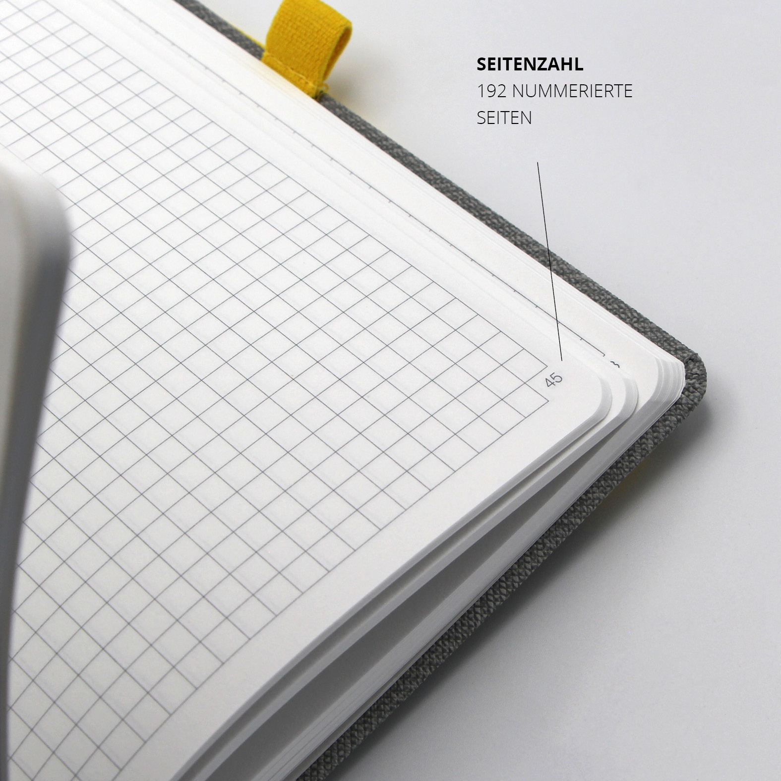 Detailaufnahme des Lanybook® Pro Notizbuchs in Tweed-Optik mit gelbem Lanyband. Gezeigt wird eine aufgeschlagene Doppelseite mit kariertem Layout und nummerierter Seite (45). Insgesamt 192 nummerierte Seiten.