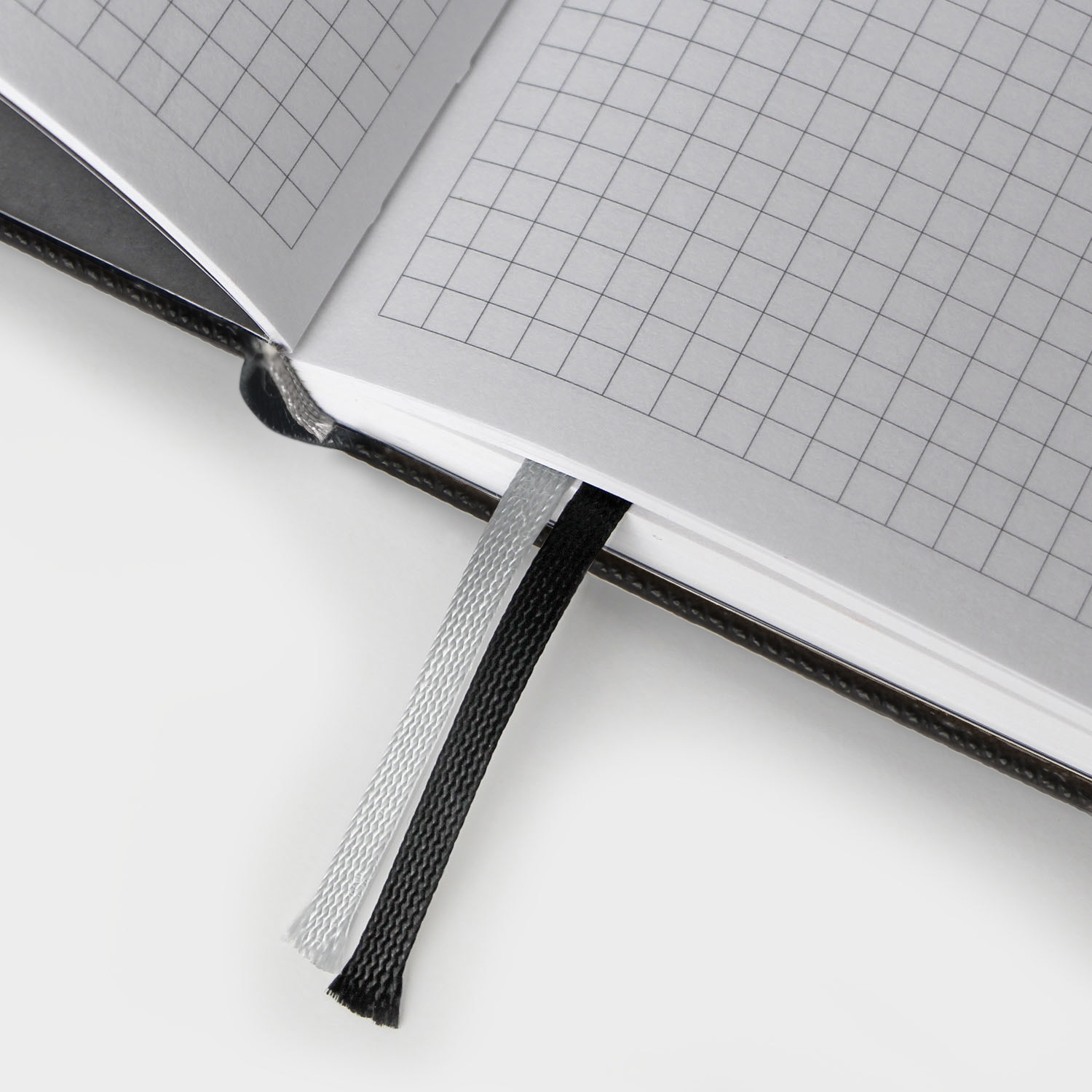 Doppelseite mit kariertem Layout und zwei gewebten Lesezeichen in Schwarz und Silber.