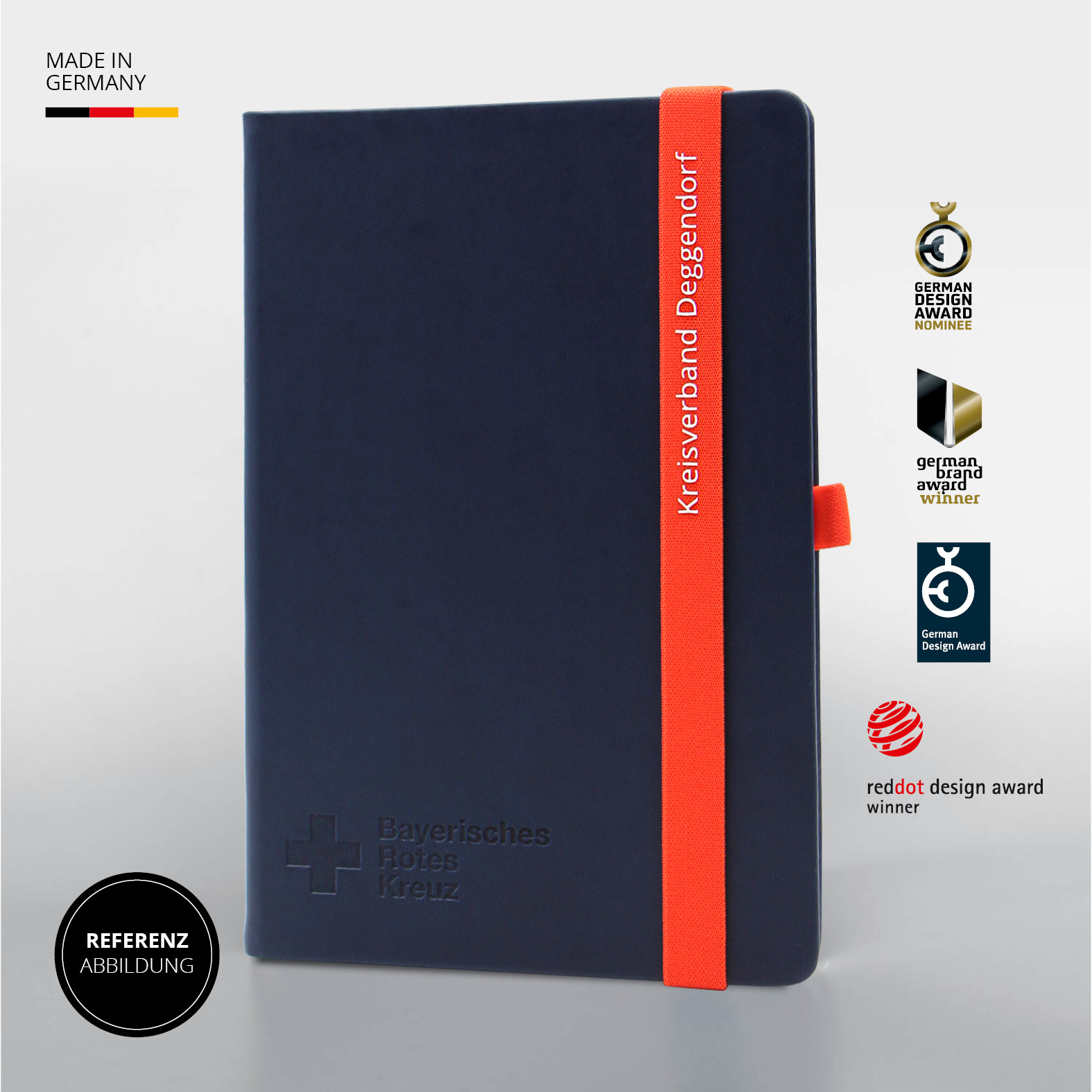 Blaues Lanybook® A5 mit rotem Lanyband® und Blindprägung „Bayerisches Rotes Kreuz“, daneben mehrere Award-Symbole (u. a. German Design Award, Red Dot Award), Kennzeichnung „Made in Germany“ oben links.