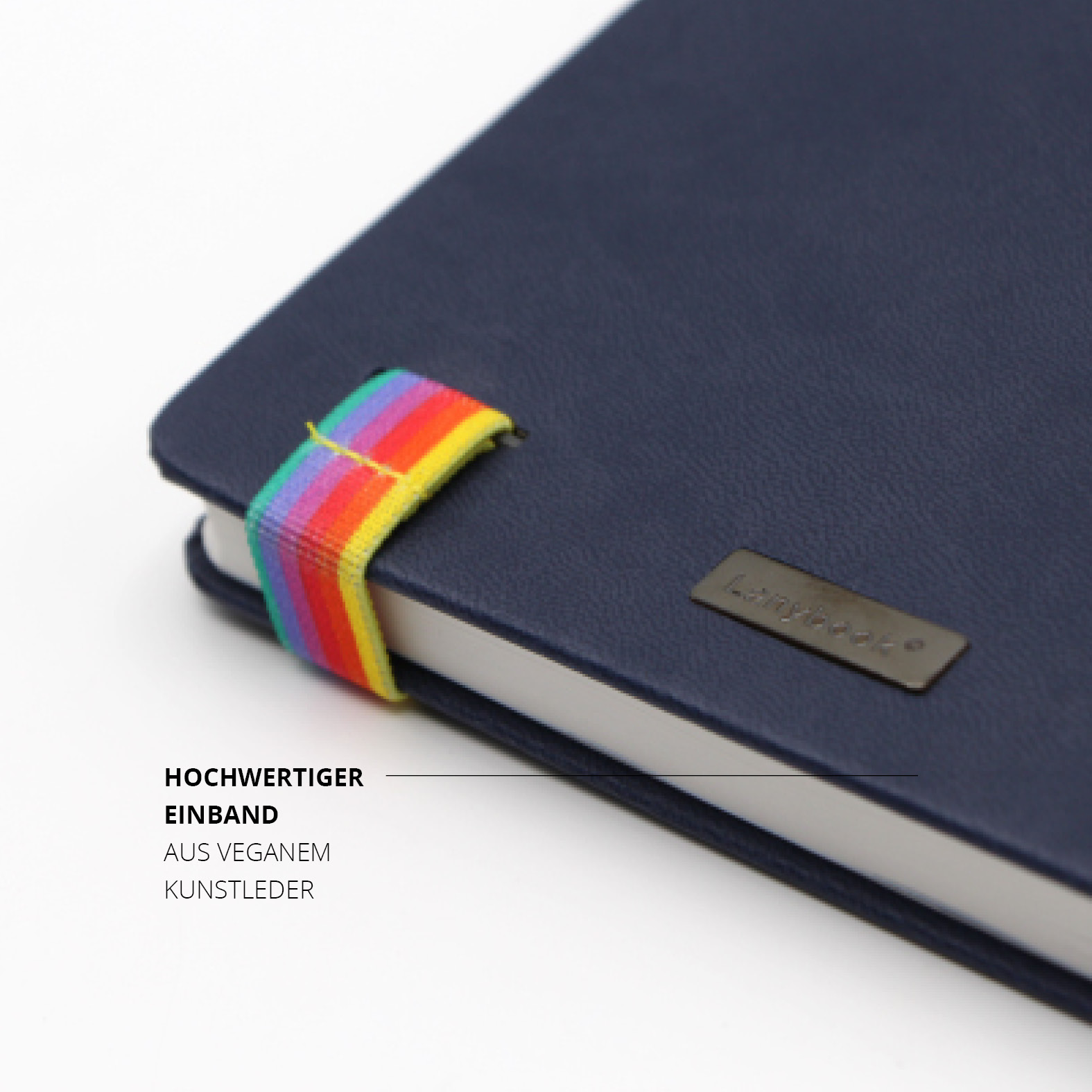 Ecke des dunkelblauen Lanybook® mit hochwertigem veganem Kunstledereinband und auffälligem, regenbogenfarbenem Gummiband. Sichtbar ist das eingelassene Metall-Label mit Lanybook®-Logo.